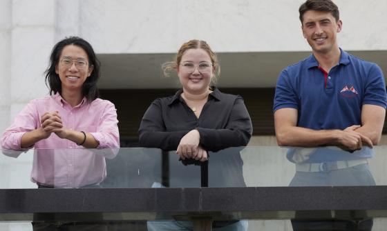 Two men and a woman leaning on the glass railing on the National Library podium and smiling