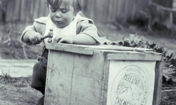 Black and white photo of a small child playing with a wooden box and a hammer