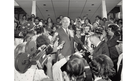 Black and white photo of Gough Whitlam speaking at Parliament House surrounded by reporters