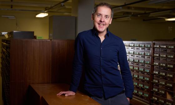 Prof. John Morrissey, 2025 National Library of Australia Stokes Fellow leaning on a table in one of the reading rooms. 