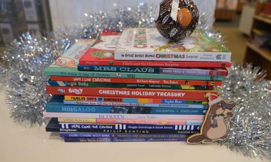 A stack of children's books including Christmas titles, decorated with tinsel