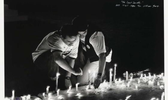 Two men kneel before rows of candles on the ground