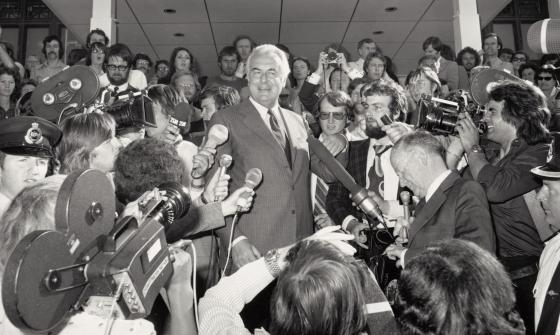 Black and white photo of Gough Whitlam speaking at Parliament House surrounded by reporters