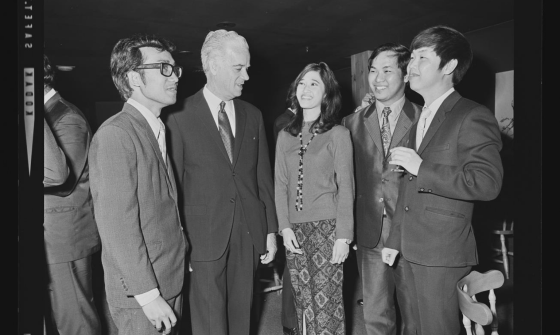 Sepia photograph of four men and a woman having a conversation in business attire.