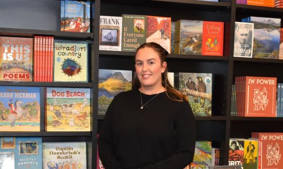 A smiling woman in a black top stands in front of a wall of books featuring NLA Publishing titles