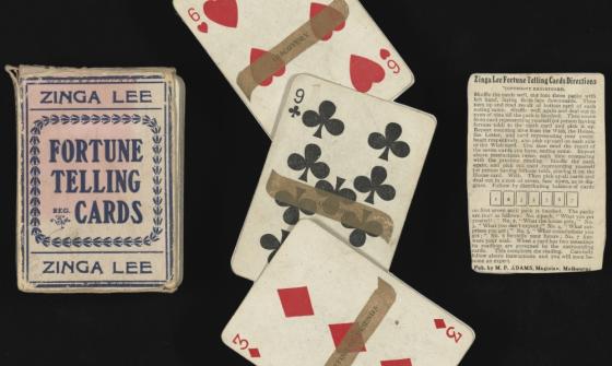 Three objects lie across this image on a black background. A card box, three playing cards with fortunes written on them, and an instruction sheet.