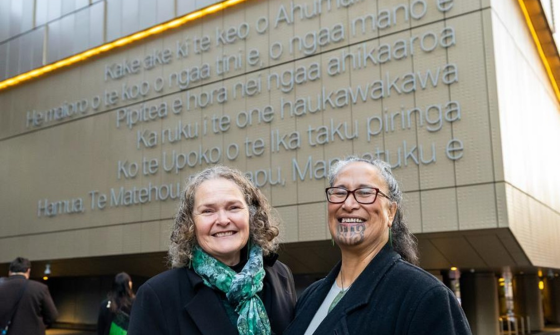 Two smiling women pictured at the front of the Archives New Zealand building