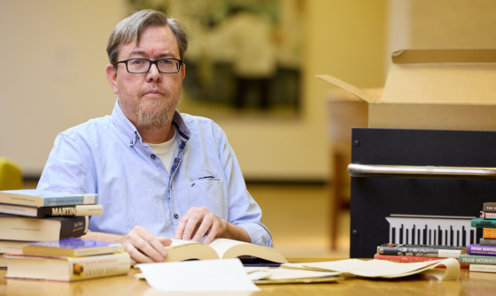 A man with glasses wearing a black button-down shirt in the National Library of Australia's Special Collections Reading Room