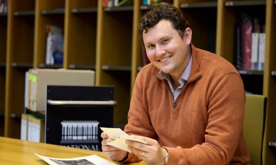 A man wearing an orange jumper while holding photographs in his hands in the Library's Special Collections Reading Room