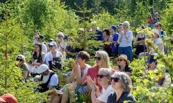 A group of people sitting in a forest, listening to a speech