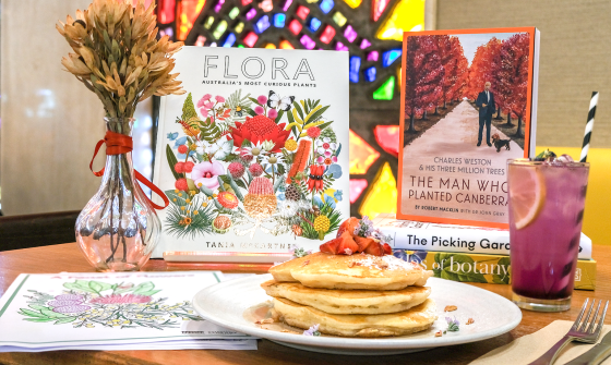 Table at Bookplate cafe with special menu items, kids activity sheets and books for Floriade with colourful stained glass windows in the background