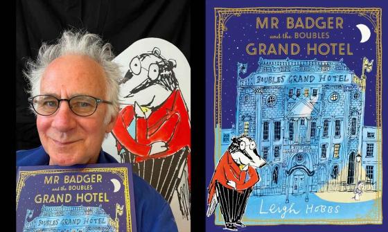 Author Leigh Hobbs poses with his children's book 'Mr Badger and the Boubles Grand Hotel'. He holds the book cover, which features an illustration of a bespectacled badger in a red jacket standing before a grand hotel under a starry night sky. Behind him, an artwork of the same badger character is visible.