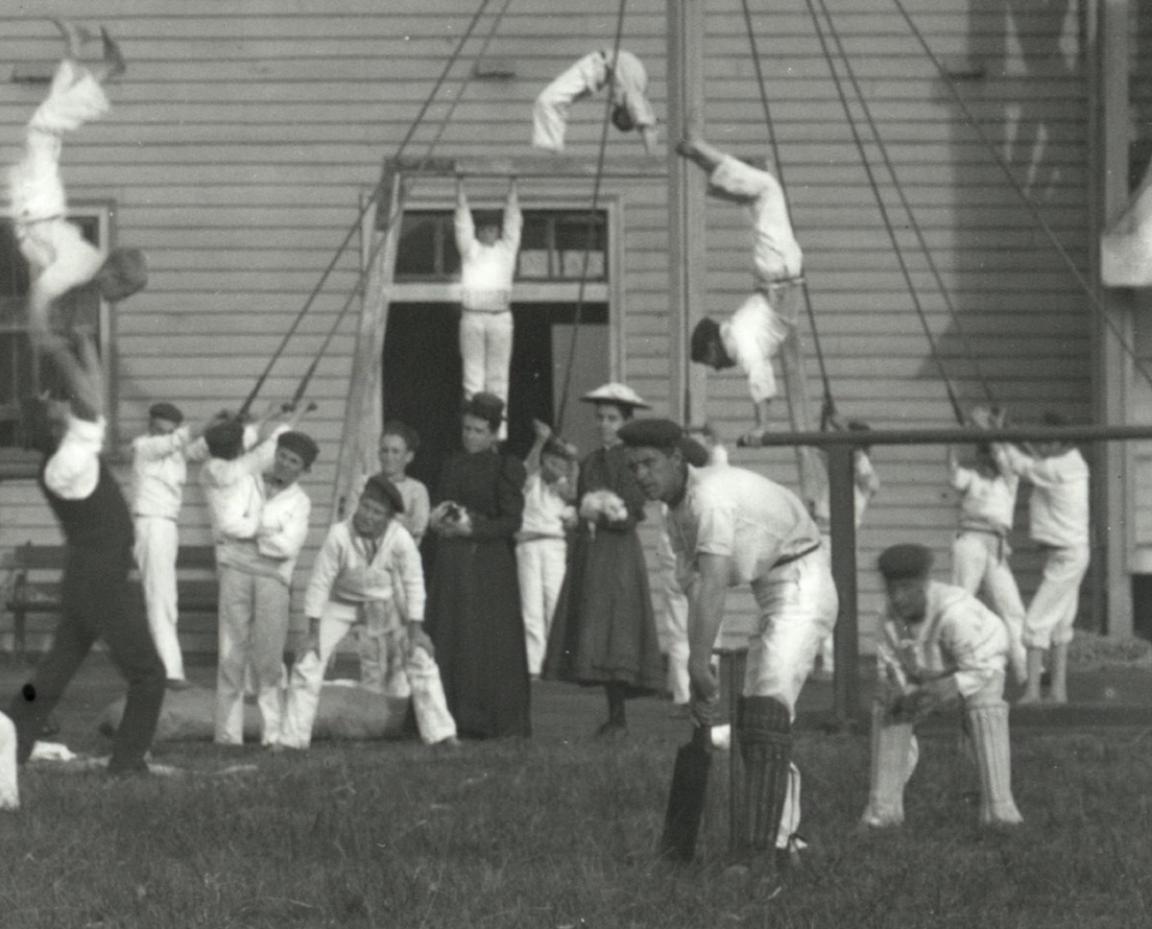 A young girl and a woman standing amongst the students of the Sobraon having recreational time playing cricket and doing gymnastics