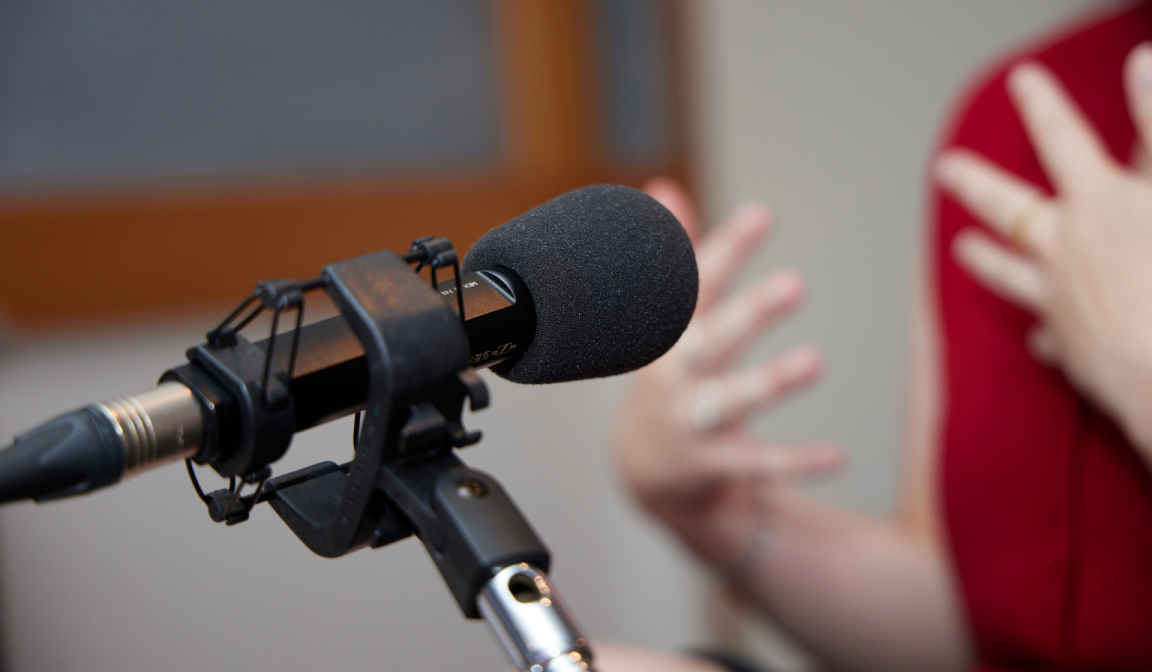 Microphone on a stand pointed towards a woman wearing red speaking and gesturing with her hands