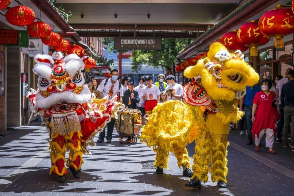 Dancers wearing tradition lion costume performing for Chinese New Year. There are two lions, one red and one yellow, with two people in each costume. Behind them stand spectators and a drummer