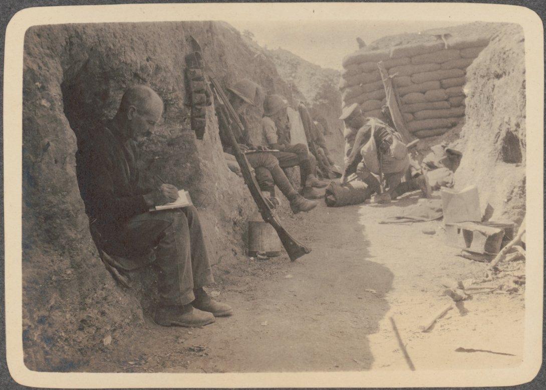 Sepia toned photo of soldiers sitting in a trench writing letters