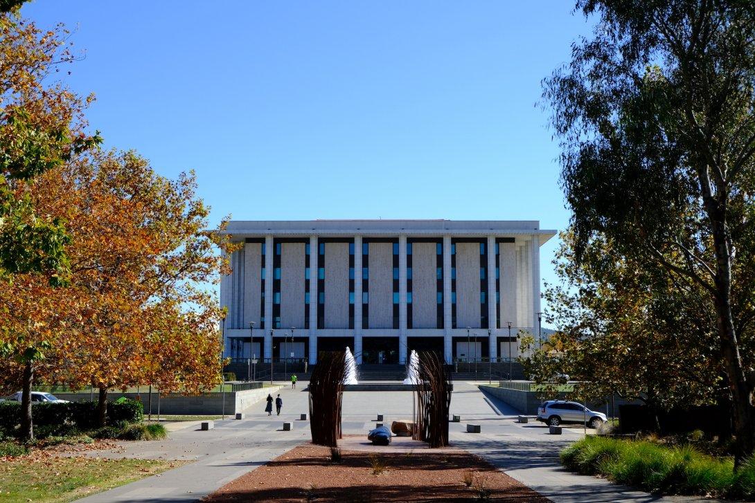 Front of the National Library building from the park across the road. The Library building is made of marble and concrete, and has large pillars along the front. It's a sunny day, and the trees are starting to change colours