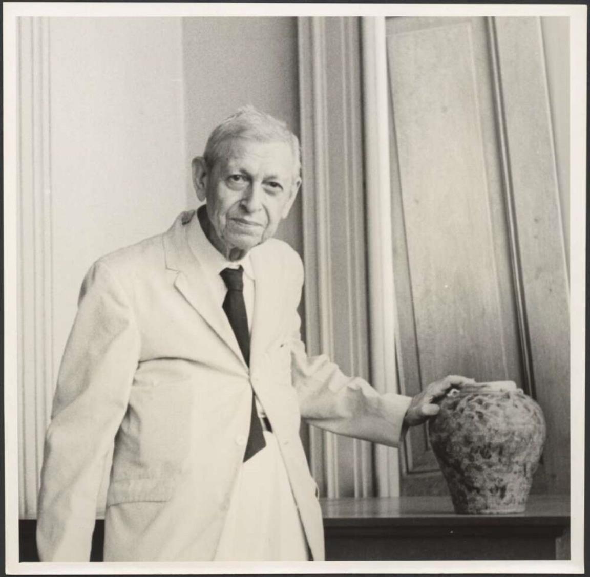 Black and white portrait of Henry Otley Beyer, standing with hand on ceramic pot wearing a white lab coat