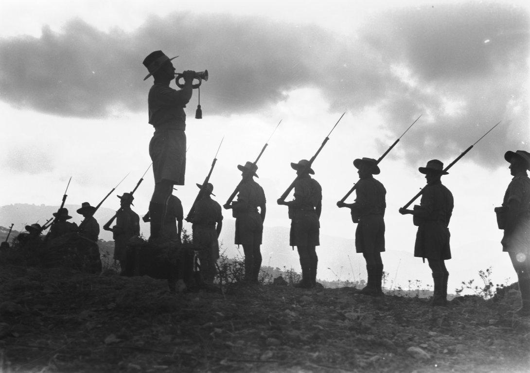 Man with a trumpet standing near a row of soldiers holding rifles over their shoulders