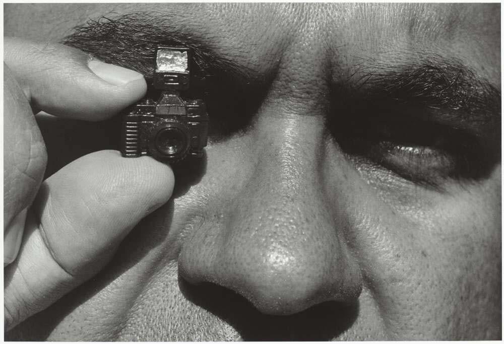 A black and white close up of a man's face showing from the brows down to just above the lip with a tiny camera covering the left eye