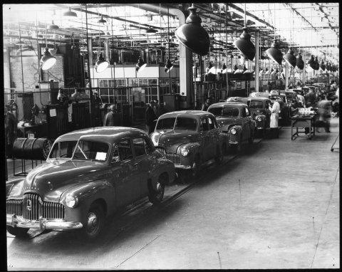 Black and white photo of a line of cars in a factory