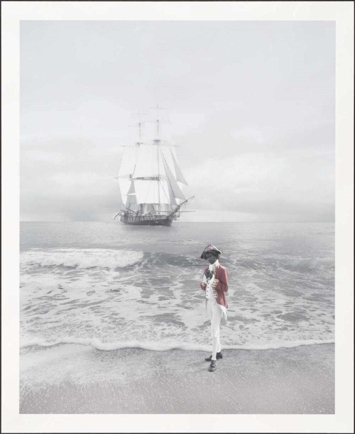 An Aboriginal person dressed in a red coat with white breeches and black boots stands on a beach, just at the edge of the water. They wear a tricorn hat with a red naval officer jacket and holds a scroll. In the background, a large, multi-masted sailing ship with white sails is anchored on calm waters under an overcast sky.