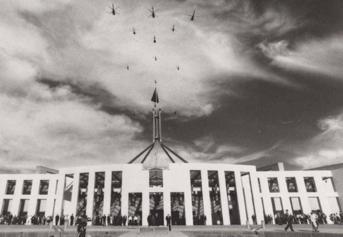 Helicopter flypast above the flagpole of Parliament House, with a crowd gathered below on the steps, Queen visible in the lower right, Canberra, 1988