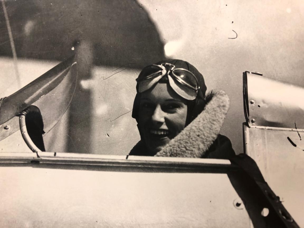 Pilot Jean Batten sitting in the cockpit of a small single-person plane smiling