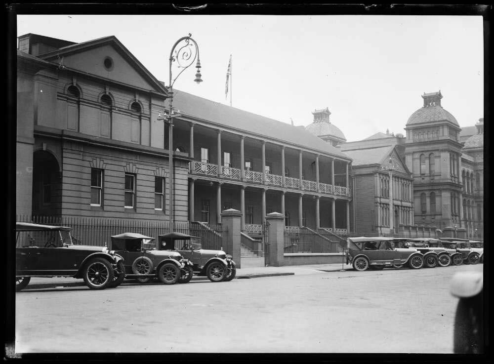 black and white photo of old buildings with old cars in the street out the front