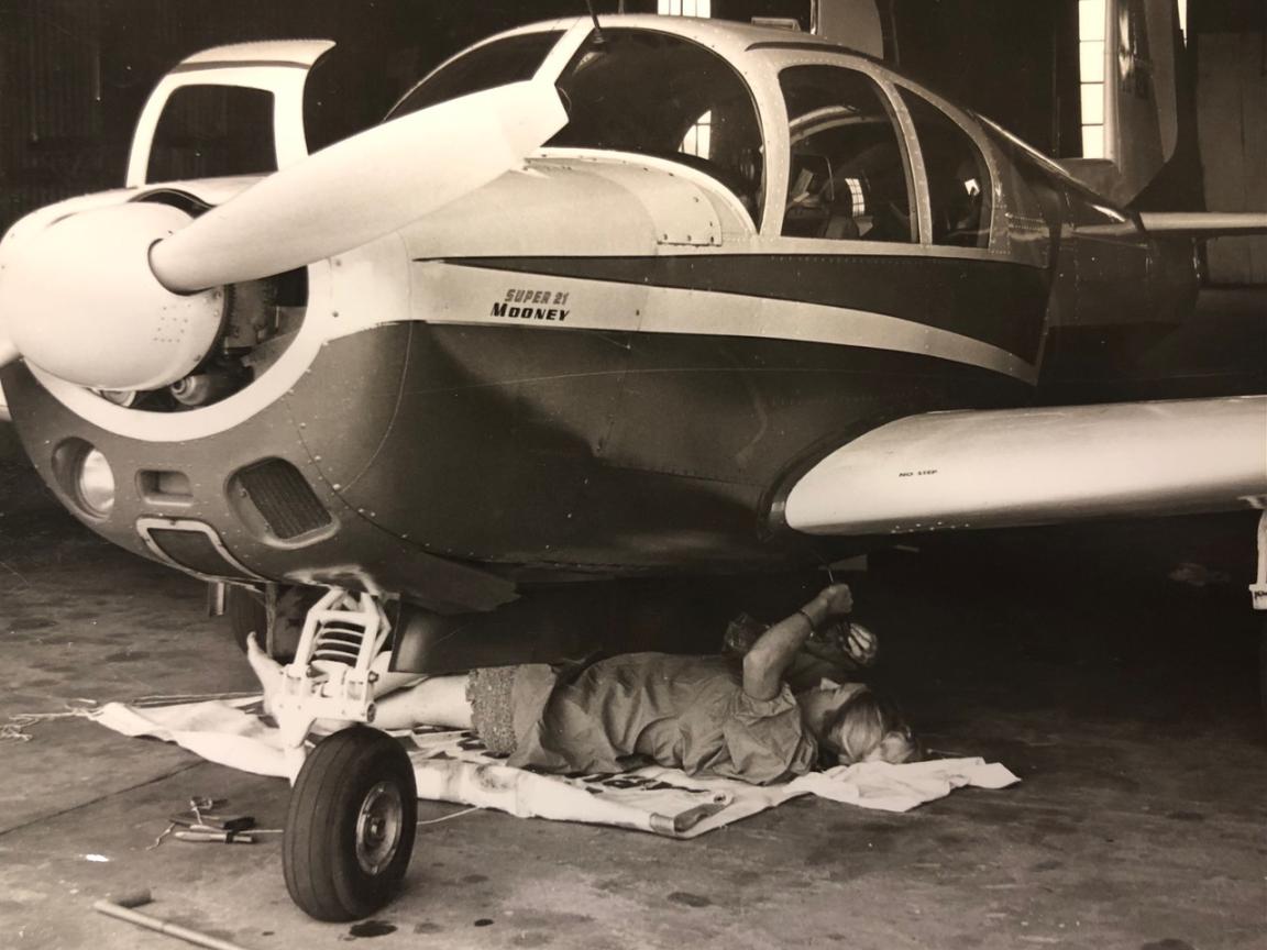 Pilot Robin Miller Dicks lying down under a plane repairing it
