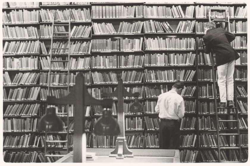 Two men, one on a ladder, looking at books on large bookshelf at the State Library of Victoria