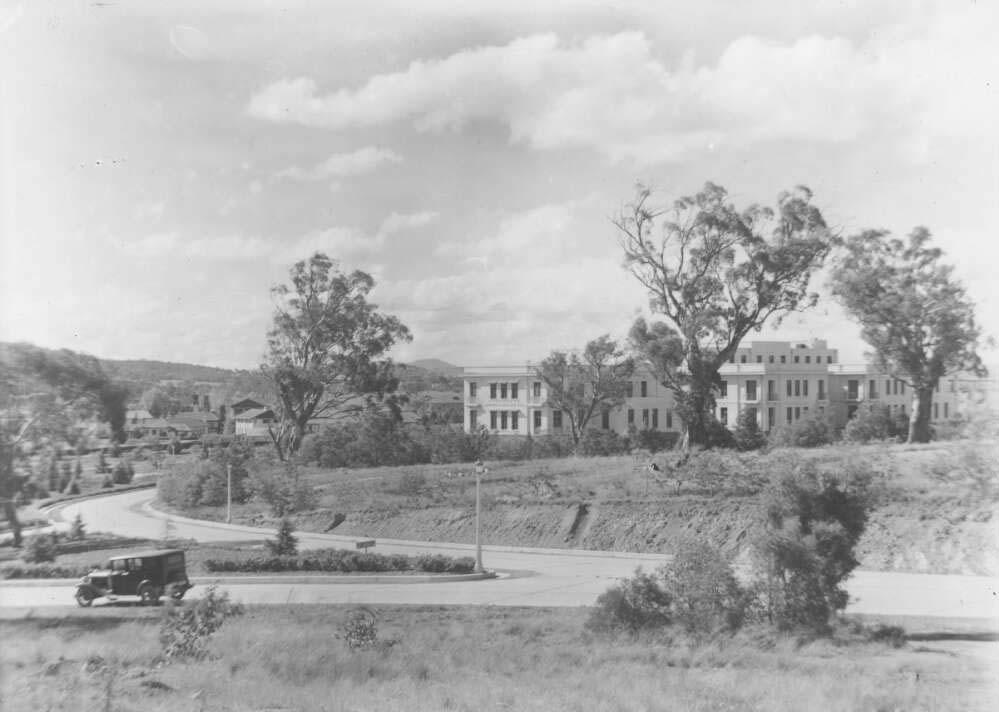 Black and white photo of a white building surrounded by trees and roads
