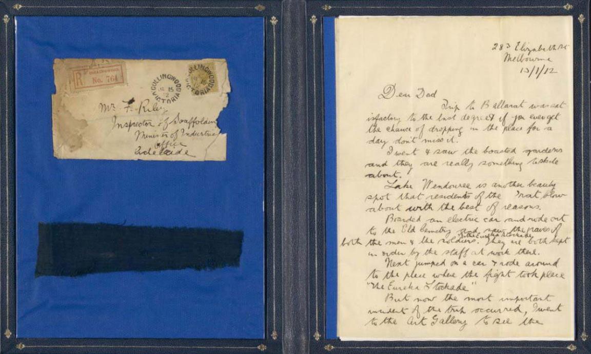 Display of an old stained, sepia coloured envelope, a sepia coloured letter and a portion of the Eureka stockade flag.