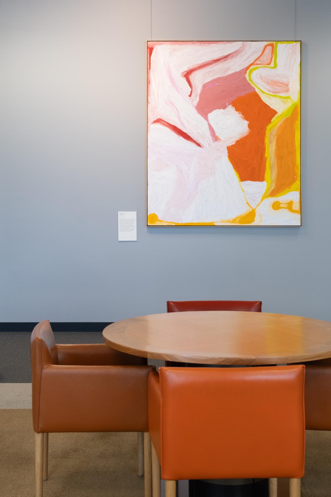 Orange chairs around a table with a large pink, orange, white and yellow painting on the wall