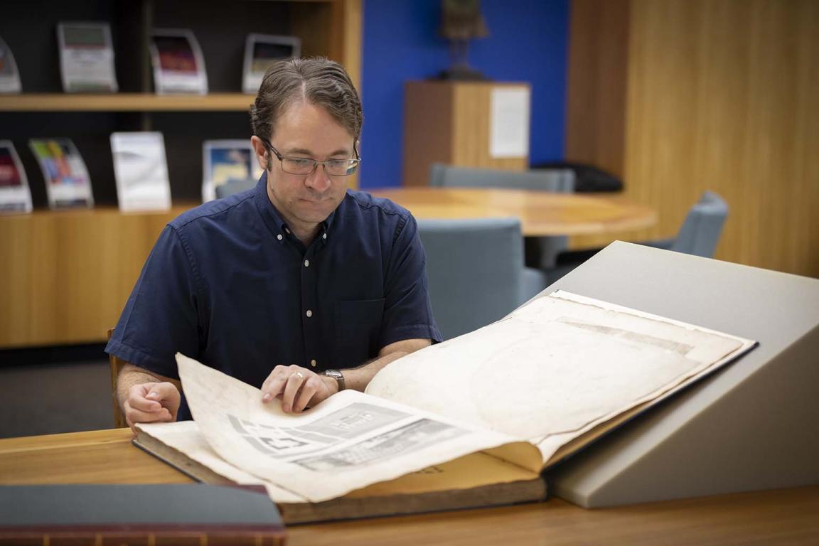 A man looking at a large open book on a desk