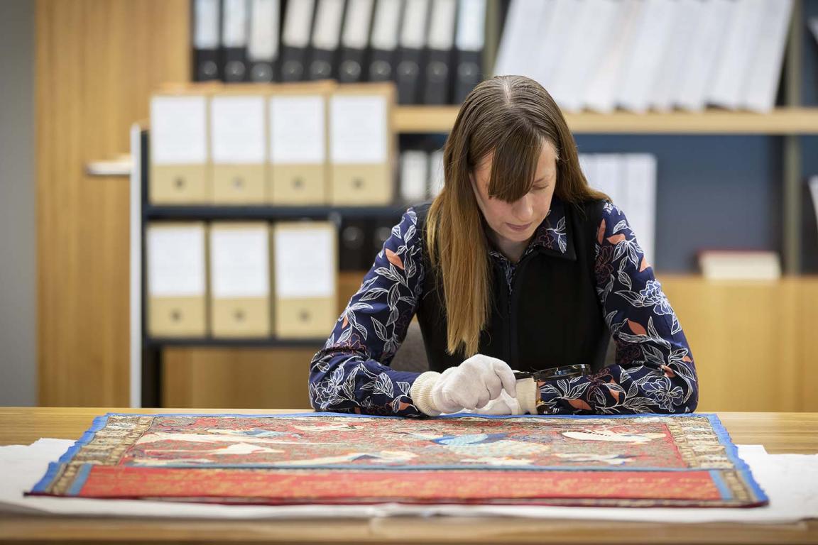 A woman wearing white gloves examining an item with a magnifying glass 