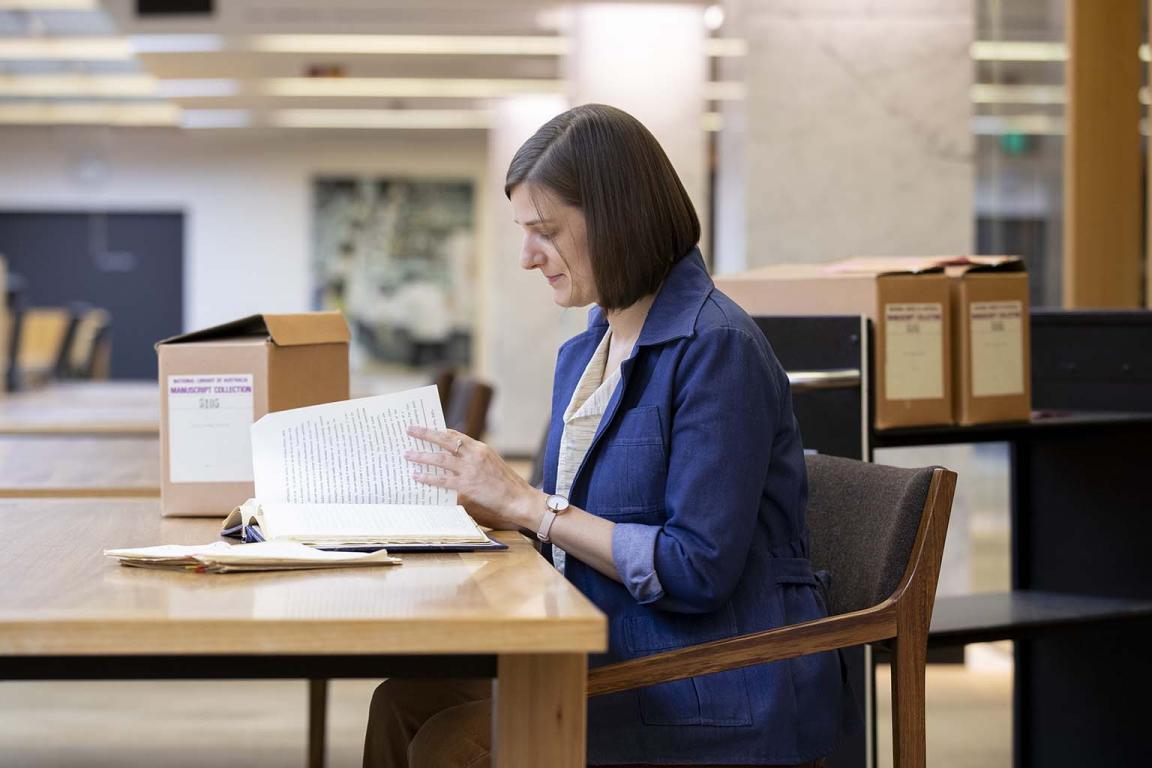 A woman turning the page in a book while sitting at a desk