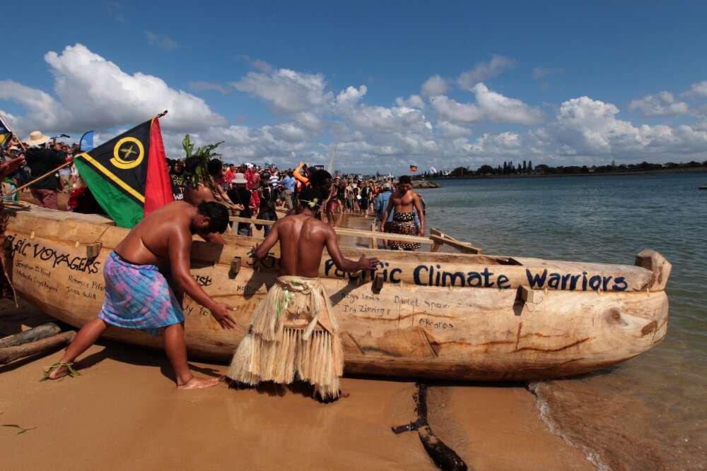 photo of a protest involving men and a canoe that has the words 'Pacific Climate Warriors' on the side