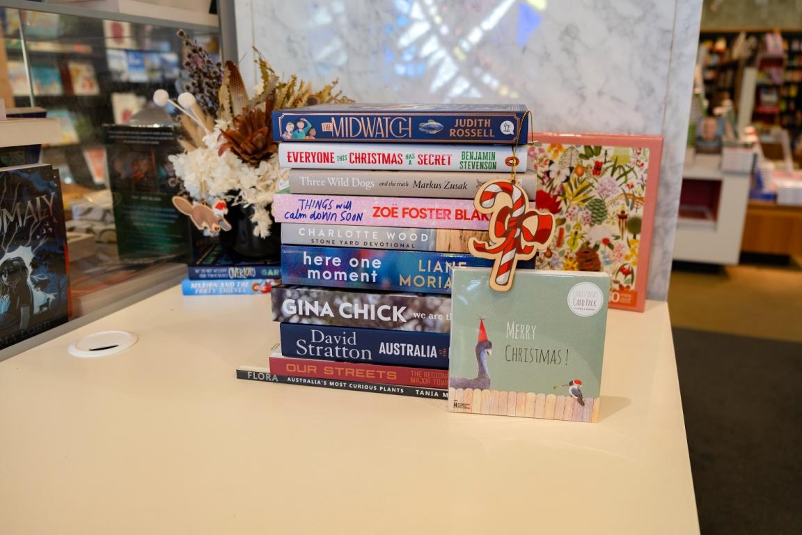 Stack of books, some with Christmas themes, with a greeting card that reads 'Merry Christmas' and a candy cane ornament