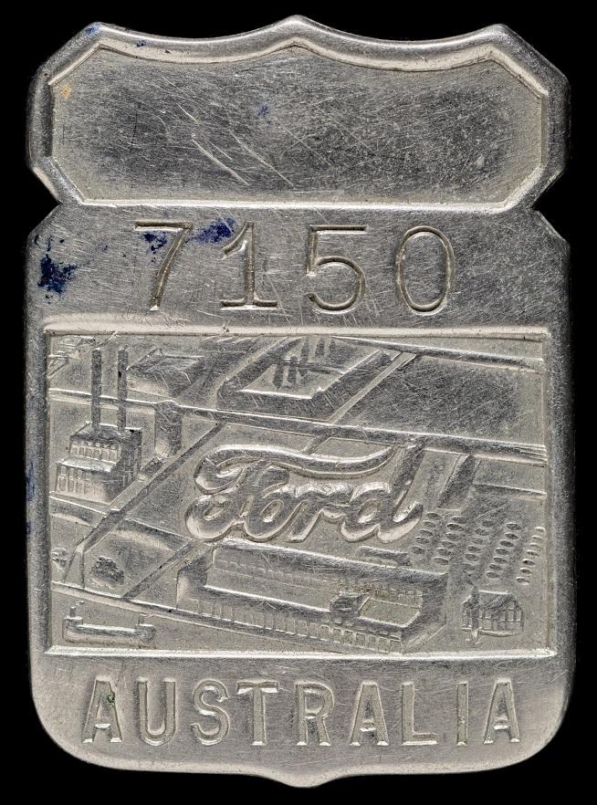 A metal badge with embossed text and imagery. The number "7150" appears at the top, followed by the word "Ford" in script style over a depiction of a factory complex. The word "AUSTRALIA" is embossed at the bottom.