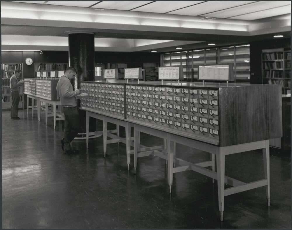 black and white photo of a man searching through a library card catalogue