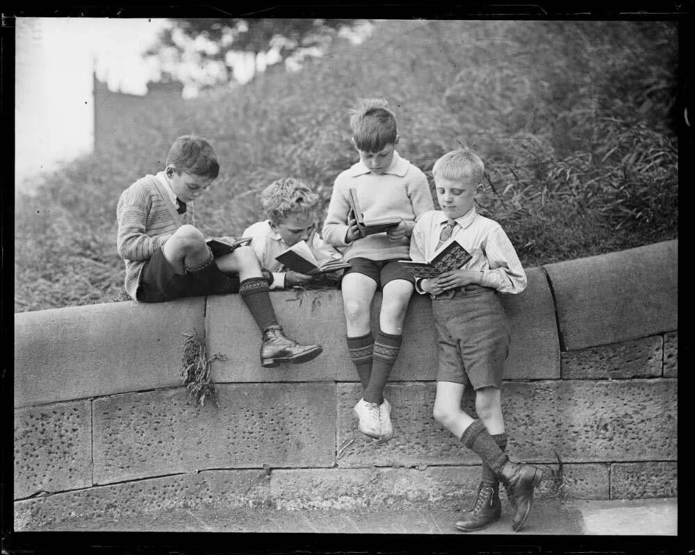 Four boys sitting on a stone wall and reading books
