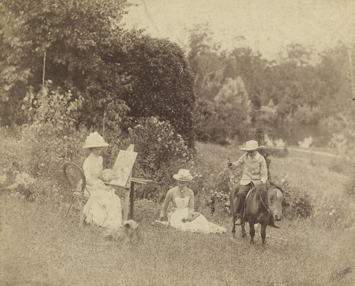 Sepia toned photo of Ellis Rowan sitting in a chair outside and making a drawing of Mary Moule who sits on the ground nearby.