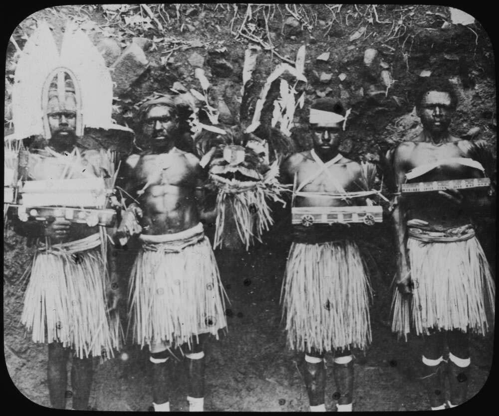 Four men in traditional dress, holding ceremonial objects