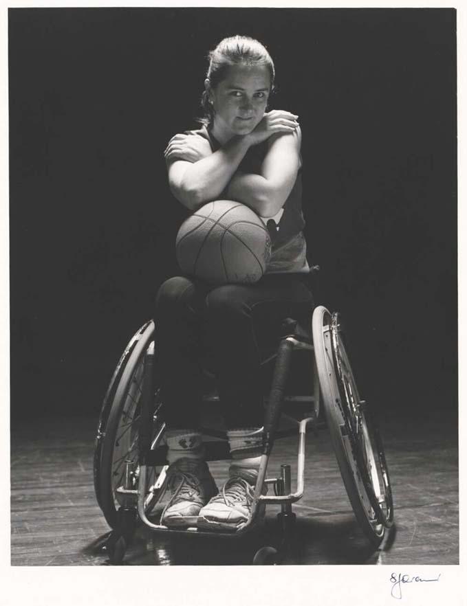 black and white photo of a woman in a wheelchair with a basketball on her lap and her arms crossed above it