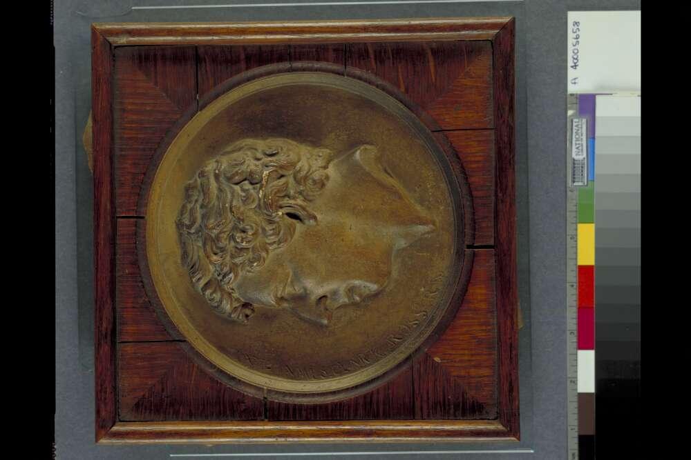 photo of a carved wooden plaque of a man's head, set on a wooden background