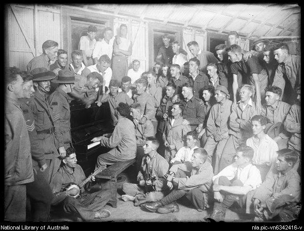 black and white photo of soldiers sitting and standing while a man plays the piano