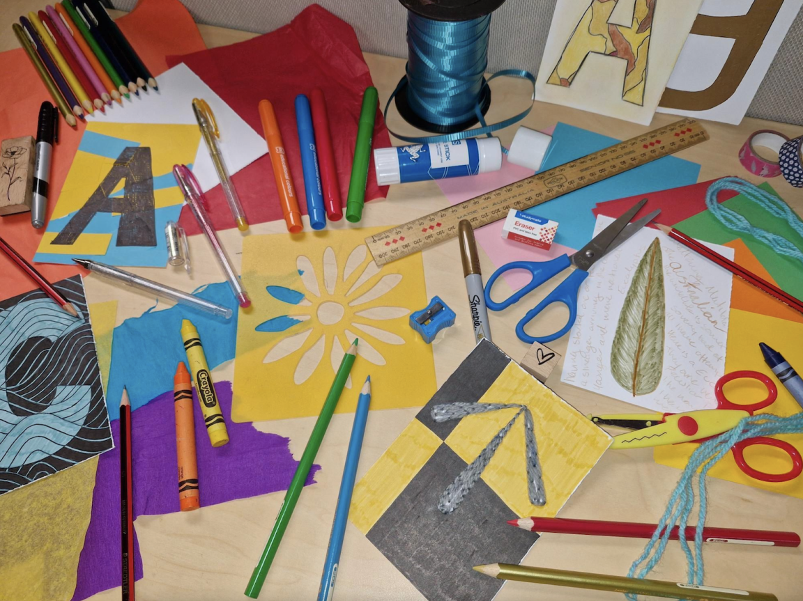 Colourful arts and crafts supplies, including markers, crayons, pencils, scissors, tissue paper, cardboard, wool and ribbon.