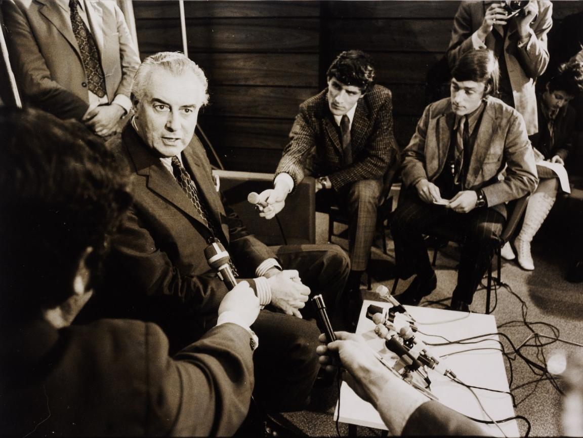 Gough Whitlam sitting and talking to men holding our microphones