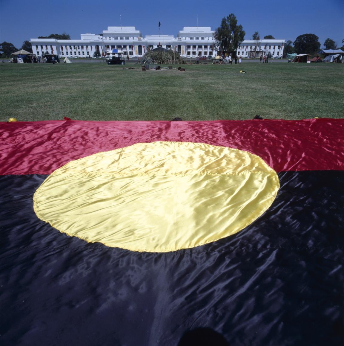 Very large Aboriginal flag laid on the grass in front of Old Parliament House